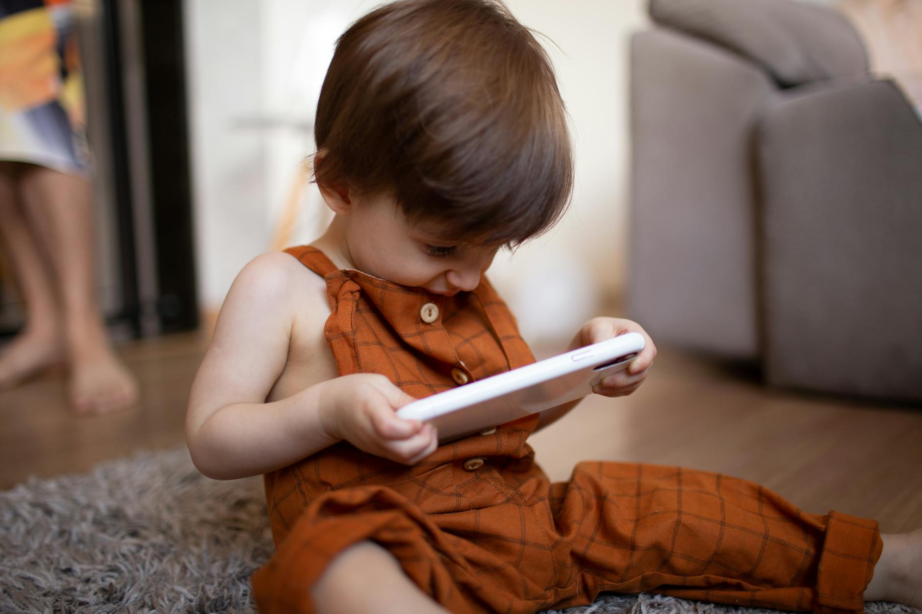 Małe dziecko w brązowym ubranku patrzy w tablet w domu Małe dziecko w brązowym ubranku patrzy w tablet w domu