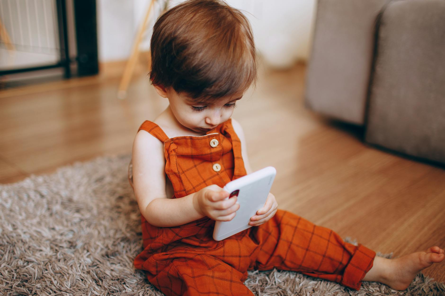 Małe dziecko w pomarańczowym ogrodniczku bawi się smartfonem w domu