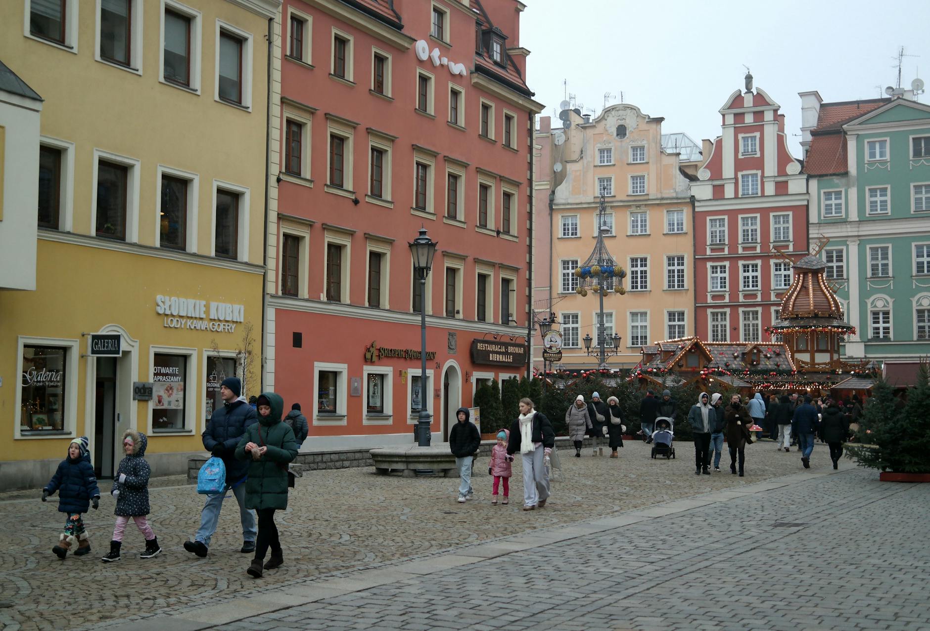 Spacer ludzi po zimowym jarmarku świątecznym między kolorowymi kamienicami