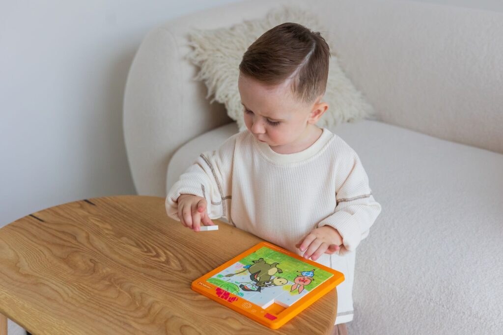 Małe dziecko układa edukacyjne puzzle przy stole w domu